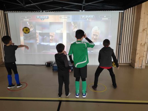 Trois enfants jouent à un jeu interactif projeté sur un mur.